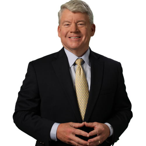 gary-bruce-headshot 1 Smiling man in a suit with a yellow tie, standing confidently with hands clasped. Professional and approachable appearance.