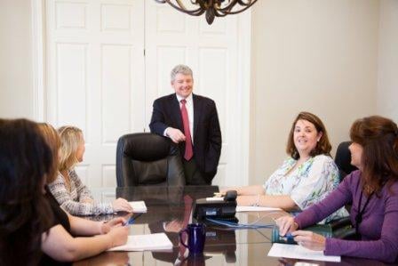 attorney Gary Bruce standing at head of conference table during staff meeting