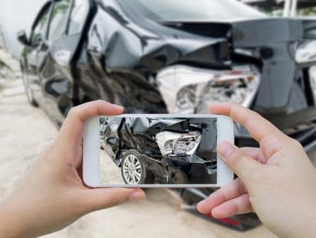 hands holding a smartphone taking a picture of a car damaged in an auto accident