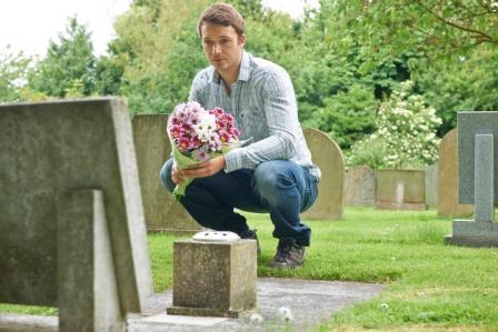 Man Placing Flowers By Headstone In Cemetery Man Placing Flowers By Headstone In Cemetery